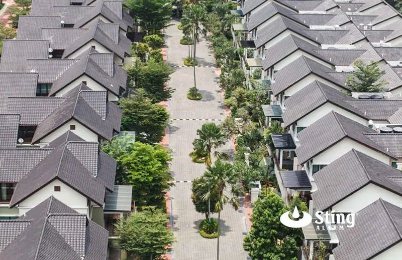 Aerial view of rows of matching townhomes with dark tile roofs along a palm-lined paved walkway