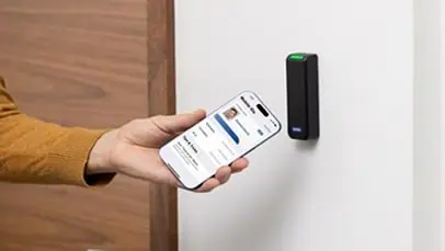 Hand holding a phone with a mobile credential up to a wall mounted access control reader