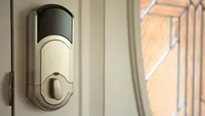 Satin nickel smart keypad deadbolt on a front door beside a leaded glass window
