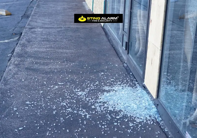 Shattered glass on the sidewalk outside a storefront with a boarded-up window panel