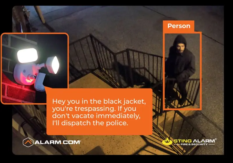 Floodlight camera spotting a person on stairs at night with a voice warning to vacate, Alarm.com and Sting Alarm logos