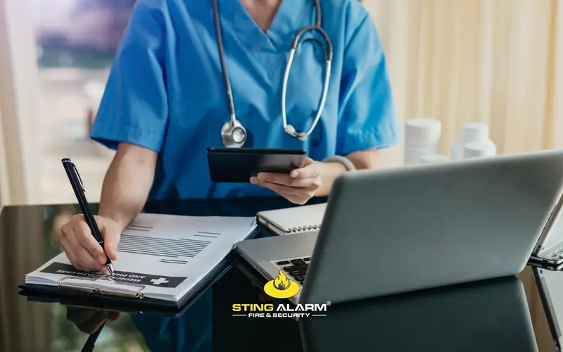 Medical professional in blue scrubs with a stethoscope taking notes and holding a tablet at a desk