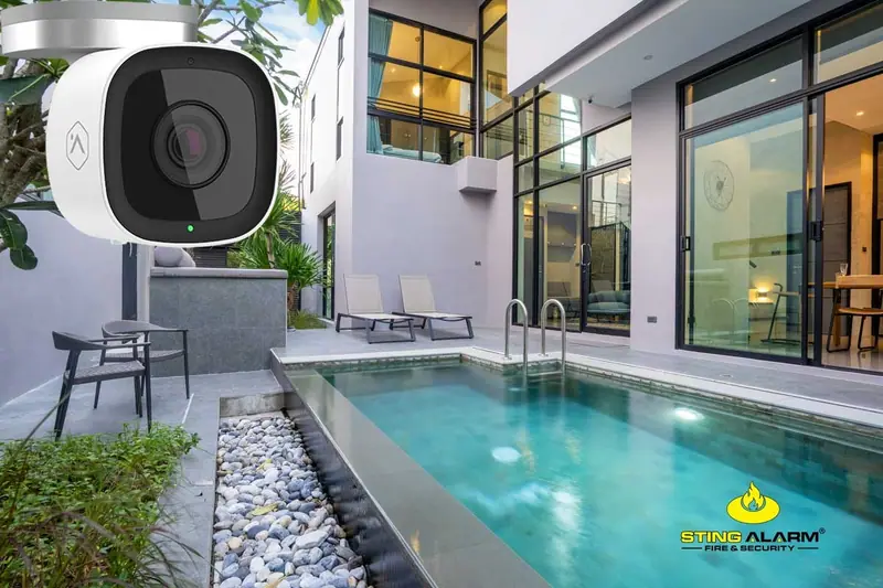 White outdoor security camera over the courtyard pool and patio of a modern two-story home