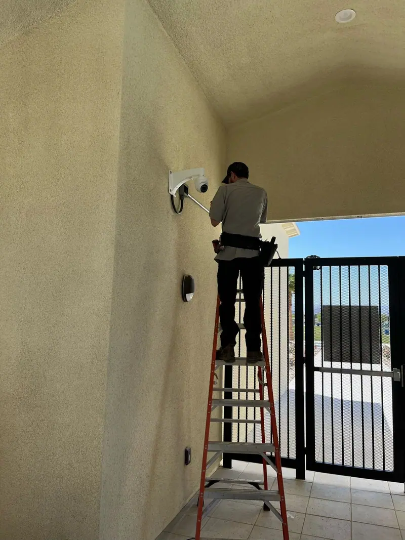 Sting Alarm technician on a ladder installing a dome security camera above a courtyard gate