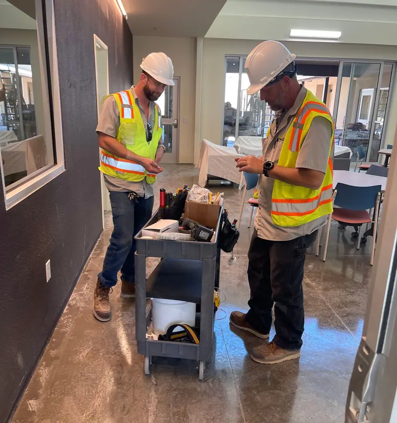 Two Sting Alarm technicians in hard hats and safety vests preparing devices on a new construction project