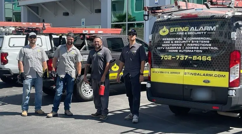 Four Sting Alarm technicians standing beside a Sting Alarm Fire and Security service van and work trucks
