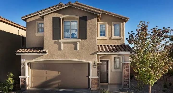 Tan two story stucco home with a tile roof, dark shutters and a two car garage under a blue sky