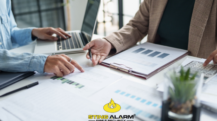 Business professionals review preparedness documents for National Preparedness Month, with the Sting Alarm logo below.